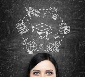 A forehead of the brunette lady who thinks about studying and graduation. Educational icons are drawn on the black chalkboard.