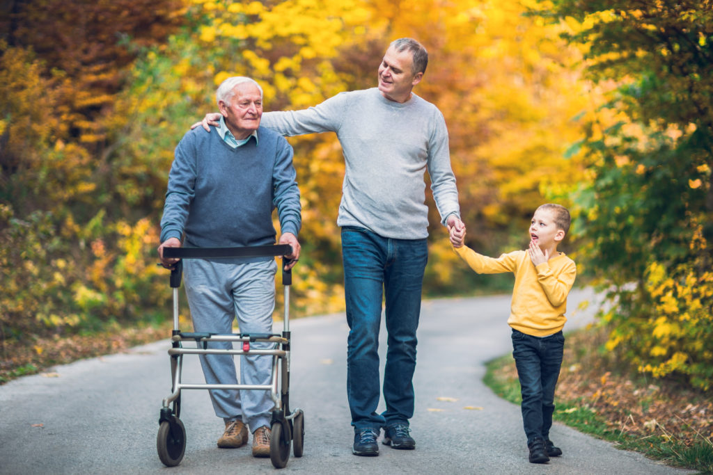 Elderly father,  adult son and grandson out for a walk in the park. Supporting family caregivers is important.