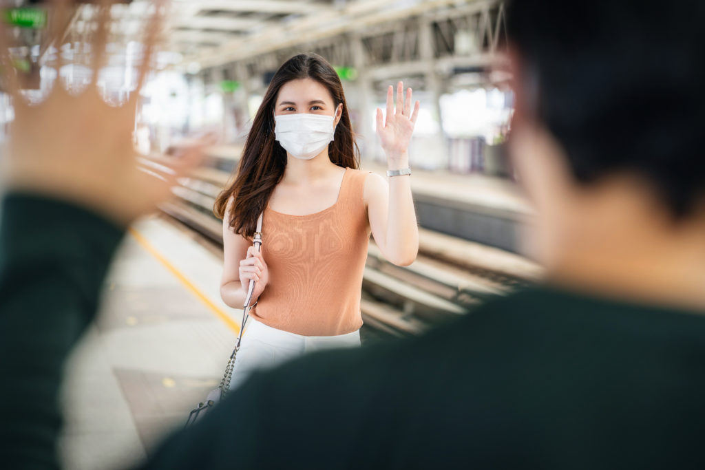 Young woman waring a mask smiling and waving to create connection with another person.