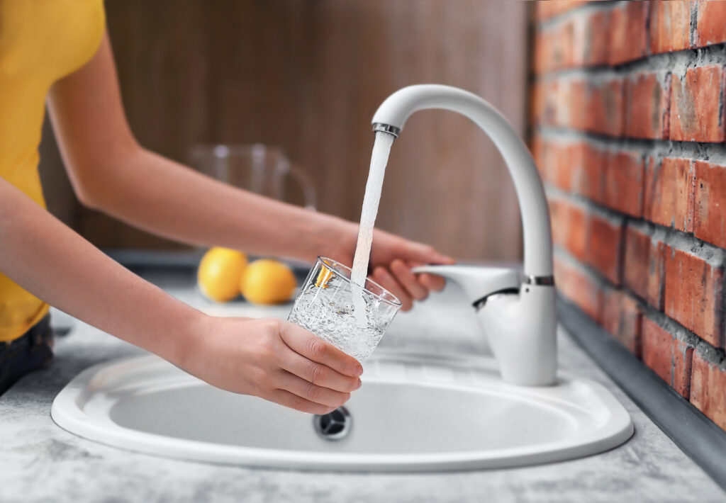 Person getting a glass of water from a kitchen faucet.