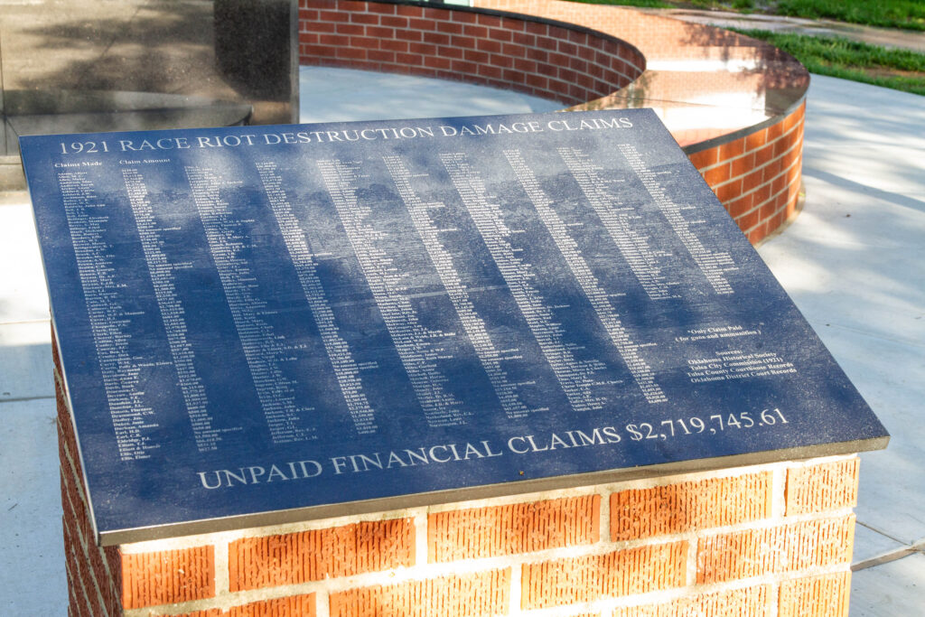 A black memorial plaque on top of a brick pillar. Words on the plaque say that the unpaid financial claims from the 1921 race riot amounted to over $2.7 million.
