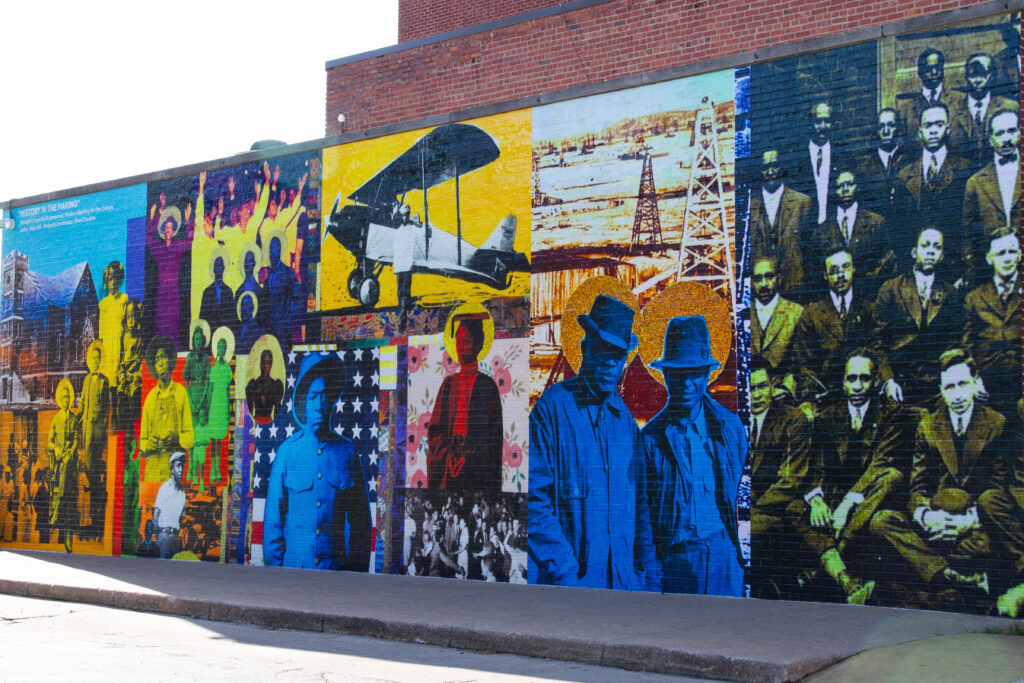 A mural painted on a building's brick wall is a colorful patchwork of portraits and historic Tulsa scenes. 
