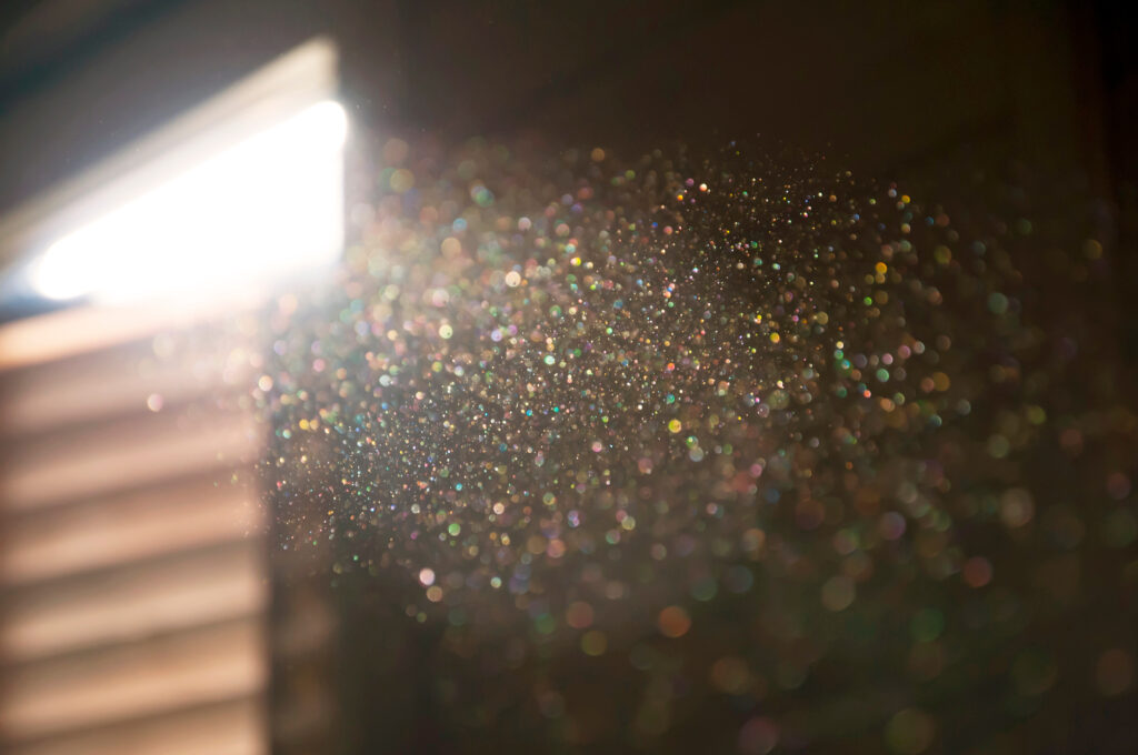 A ray of sun coming through the wooden shutters, illuminates dust on the inside of a dark room. Close up, selective focus. Vintage background. This image is licensed from Adobe Stock.