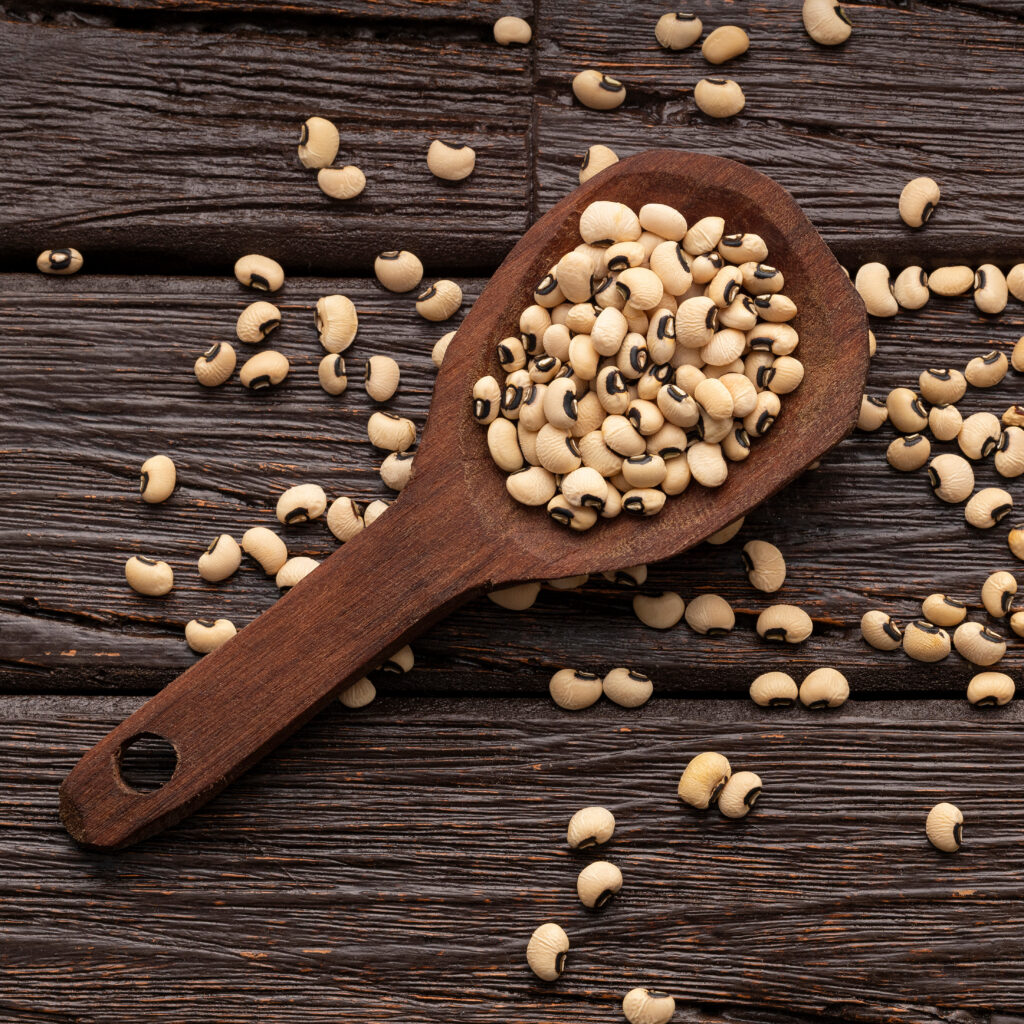A dark background with a wooden spoon holding tan and black beans scattered on the spoon and on the background.
